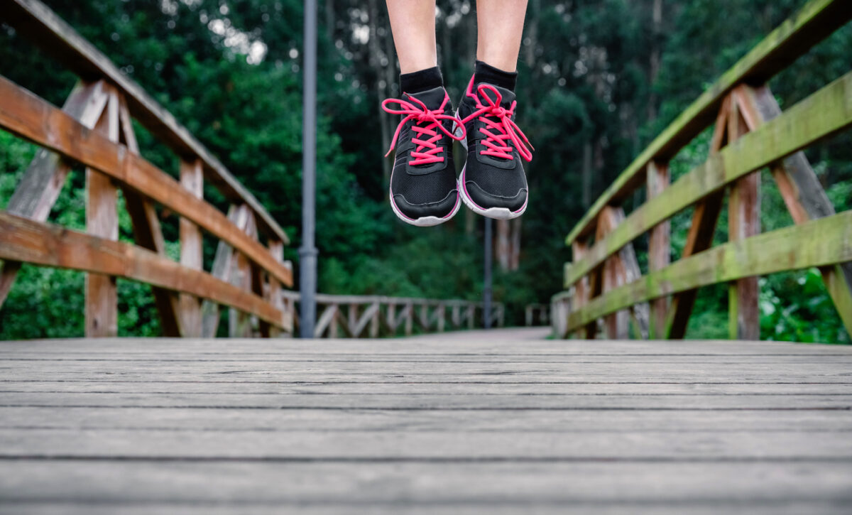 a woman jumps on a wooden bridge. we see only her running shoes with bright pink laces